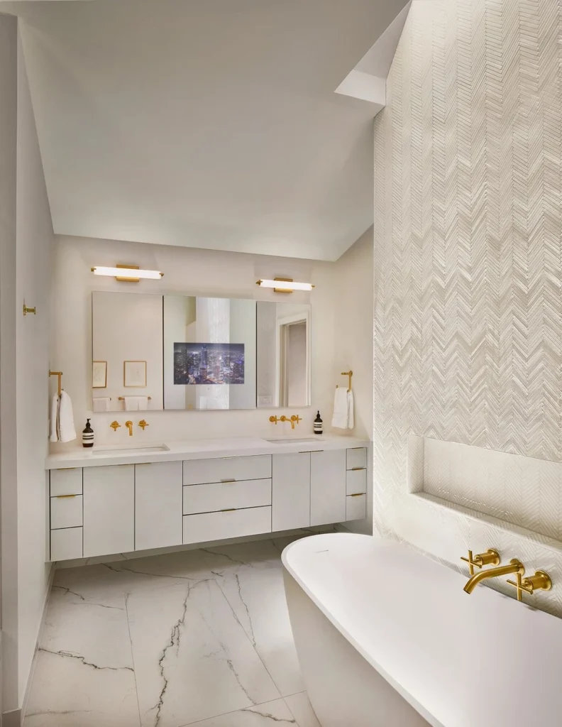 White bathroom with long vanity, freestanding tub, gold fixtures, and herringbone tile in Eudora