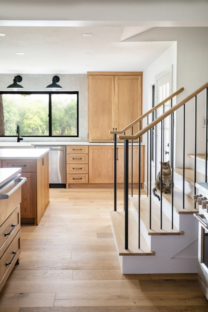 Light-filled kitchen with natural wood cabinetry, wide-plank flooring, and integrated staircase