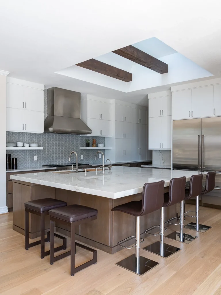 Open white kitchen with waterfall island, dark stools, and exposed wood beams in Harbor Town I