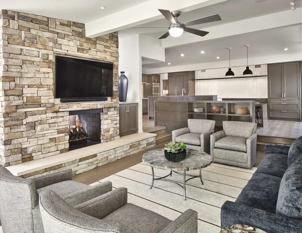 Open living room with stone fireplace and contemporary kitchen beyond in the Yamini remodel