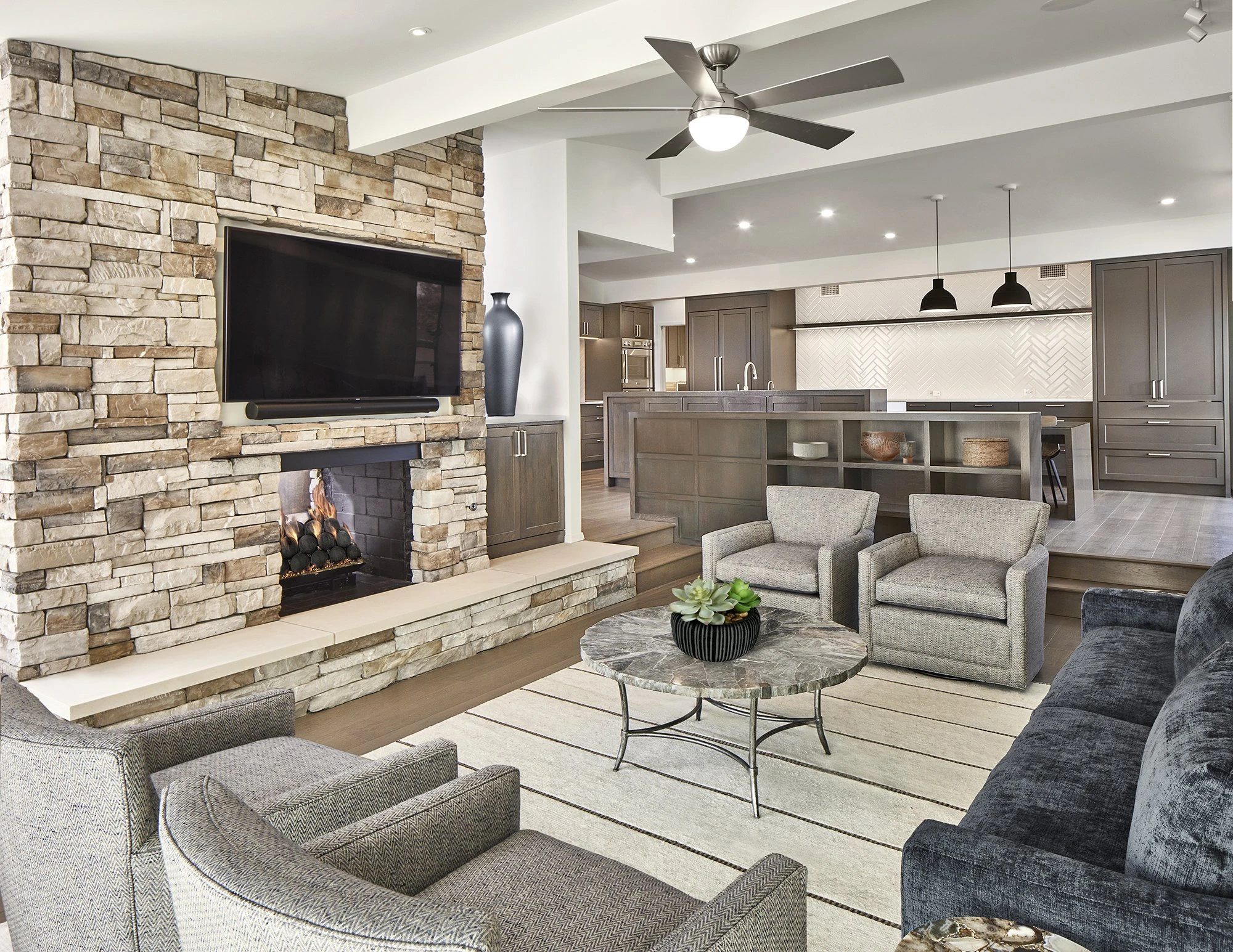 Open living room with stone fireplace and contemporary kitchen beyond in the Yamini remodel